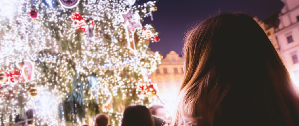 December post image - lady standing in front of Christmas tree with lights